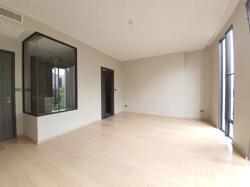 Condominium for sale in Huai Khwang, Bangkok - Master bedroom with glass-walled ensuite, pale wood flooring and tall windows.