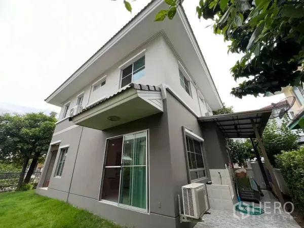 Detached House for sale in Bang Kruai, Nonthaburi - Two‑storey detached house exterior with sliding glass doors, side canopy and green lawn.