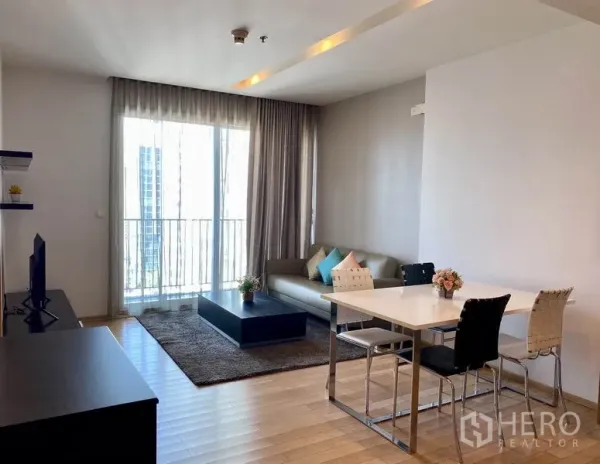 Condominium for rent in Khlong Toei, Bangkok - Bright living and dining area with floor-to-ceiling windows, balcony view and wood flooring.