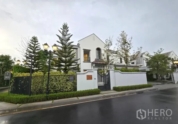 บ้าน ให้เช่าในSaphan Sung, Bangkok - ด้านหน้าบ้านเดี่ยวสองชั้นหรู ประตูรั้วเหล็ก ผนังสีขาวและต้นไม้สูง
