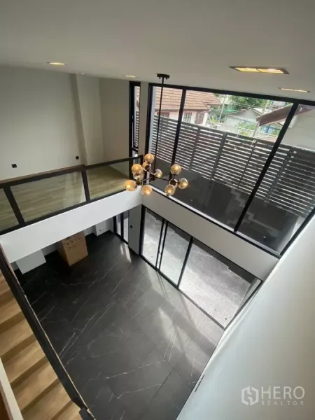 Townhouse for rent in Huai Khwang, Bangkok - Double-height living area with black marble floor, full-height windows and a modern chandelier.