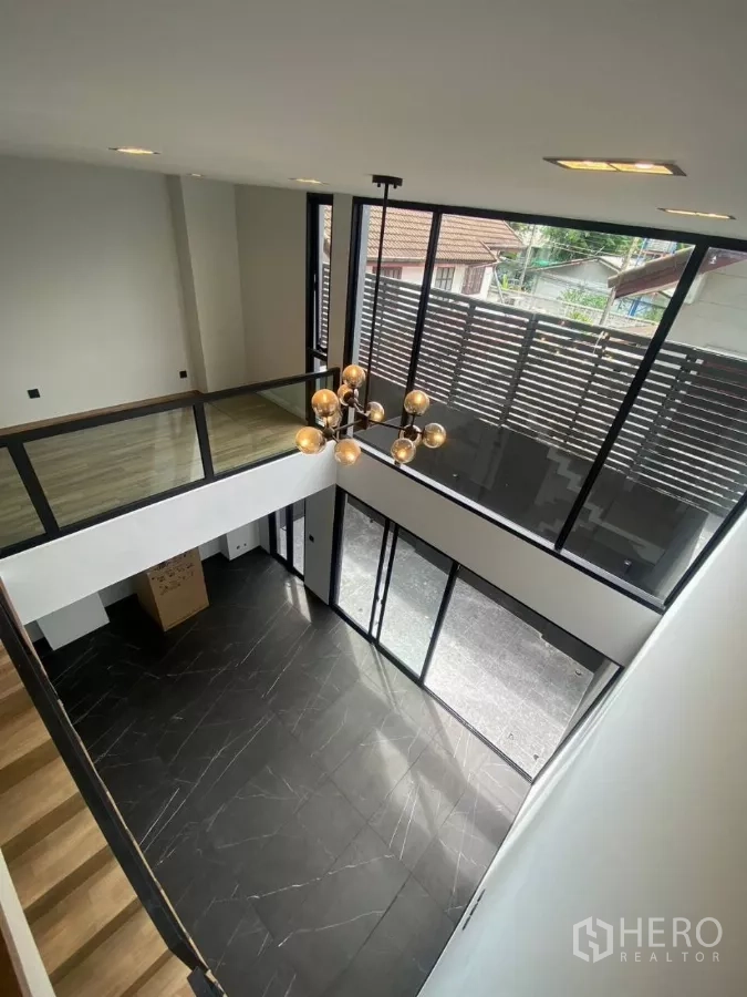 Townhouse for rent in Huai Khwang, Bangkok - Double-height living area with black marble floor, full-height windows and a modern chandelier.