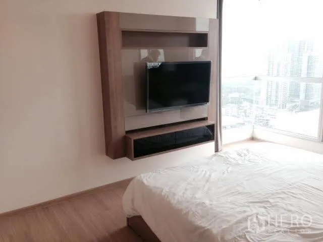 Condominium for rent in Khlong Toei, Bangkok - Bedroom with wall-mounted TV unit and floor-to-ceiling windows showcasing city views.
