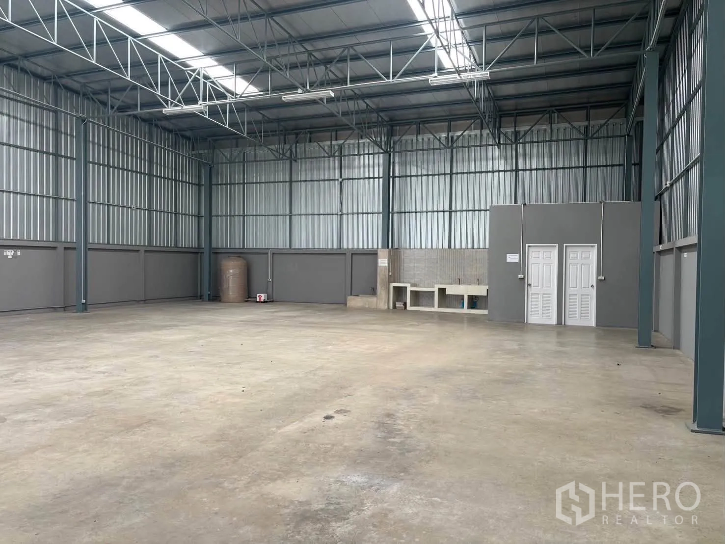 仓库 for rent in Mueang Pathum Thani, Pathum Thani - 宽敞仓库地面，金属围护，屋顶采光板，操作台与水箱，旁有两扇卫生间门。