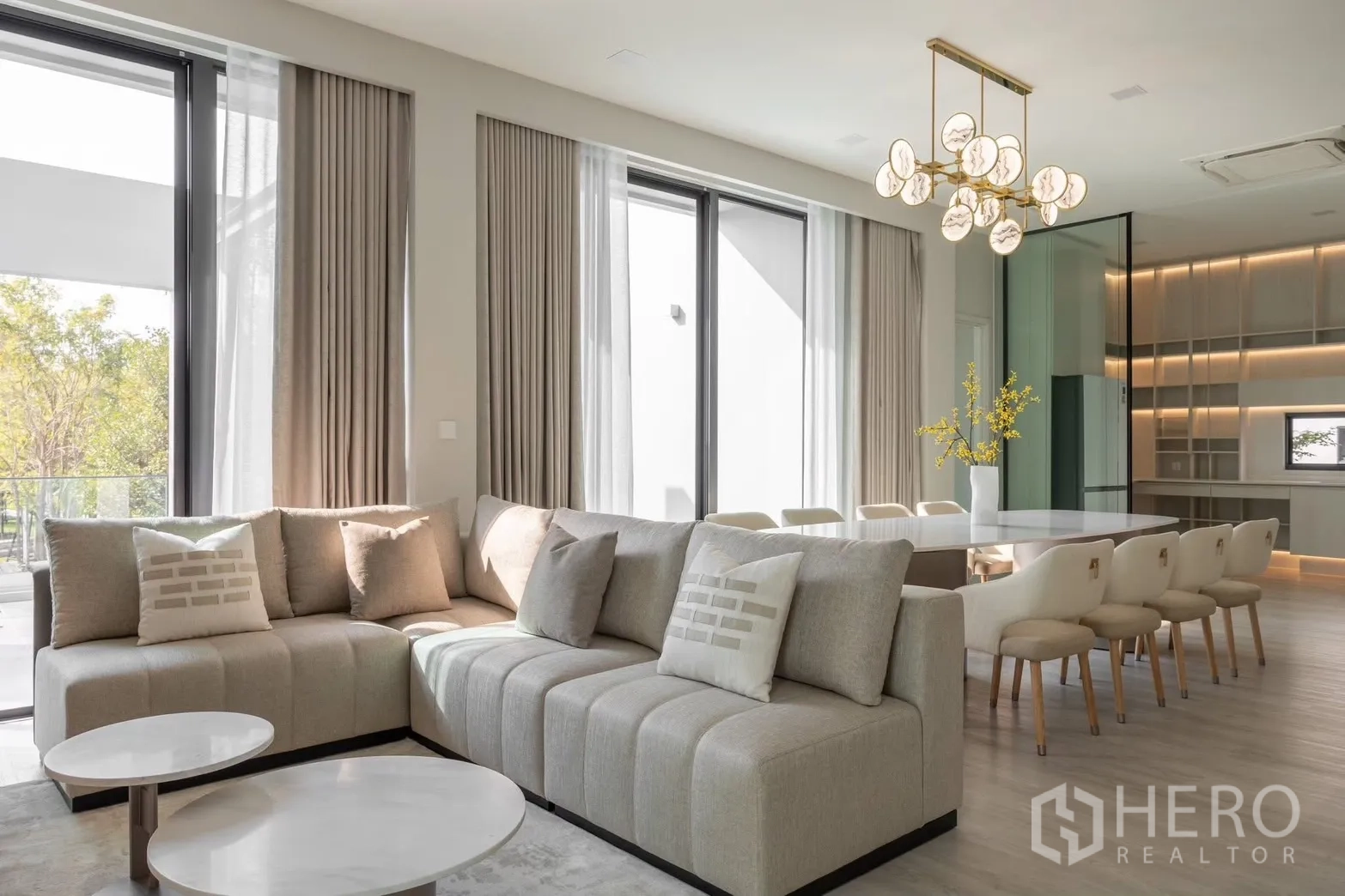 Detached House for rent in Saphan Sung, Bangkok - Sunlit living room with L-shaped sofa, floor-to-ceiling windows, and adjoining dining zone.