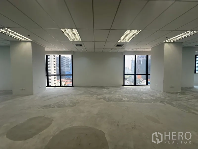 Office Space for rent in Bang Rak, Bangkok - Bright office floor with large windows, city views and fluorescent lighting over a concrete subfloor.