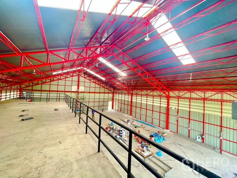 Warehouse for rent in Lam Luk Ka, Pathum Thani - View from the mezzanine over a high-clearance warehouse with red steel roof structure.