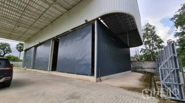 Warehouse for rent in Mueang Nonthaburi, Nonthaburi - Covered loading bay with wide sliding metal doors and a concrete apron at the warehouse entrance.