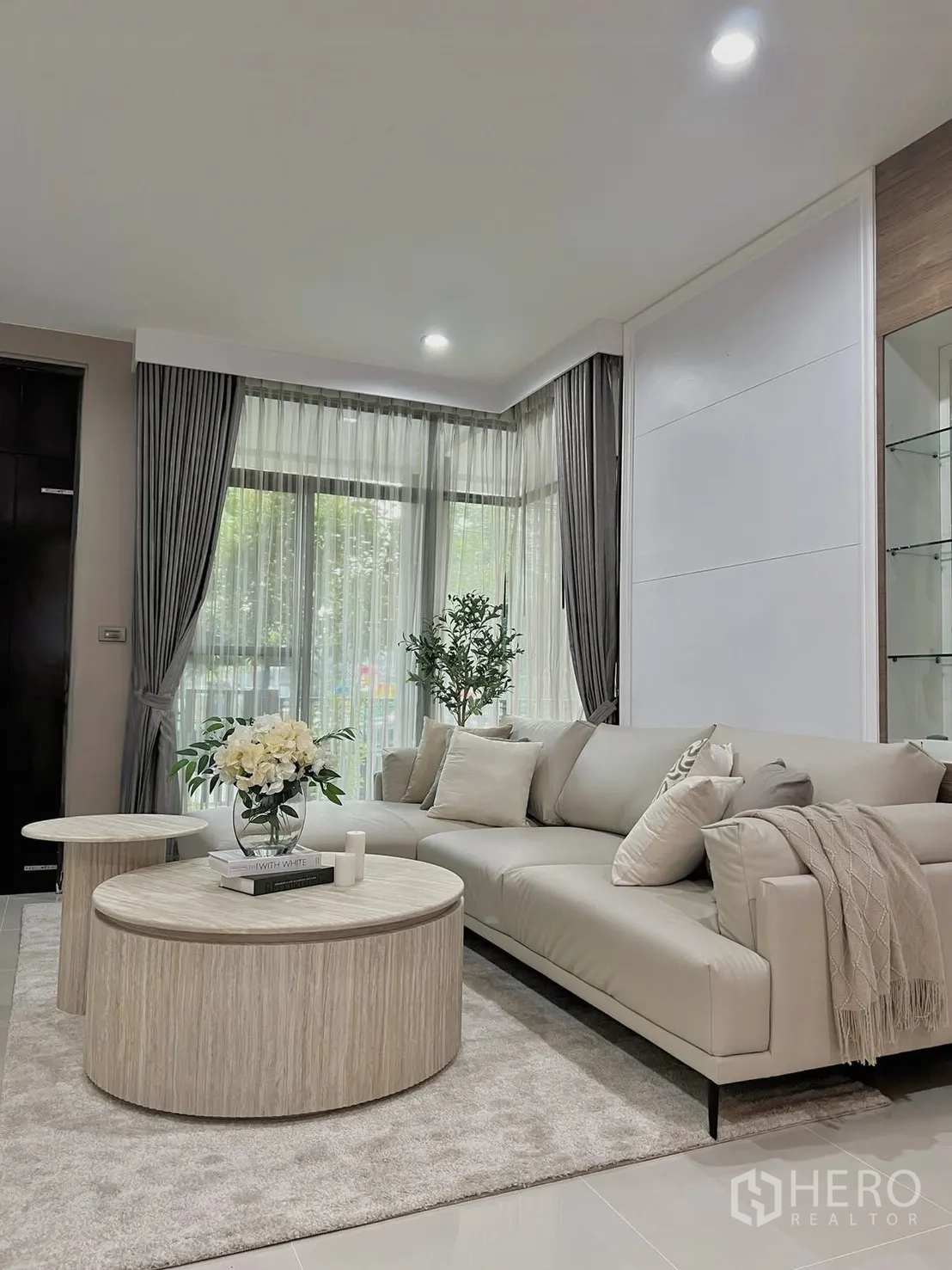Detached House for rent in Prawet, Bangkok - Spacious living room with an L-shaped sofa, round coffee tables, and floor-to-ceiling curtains.