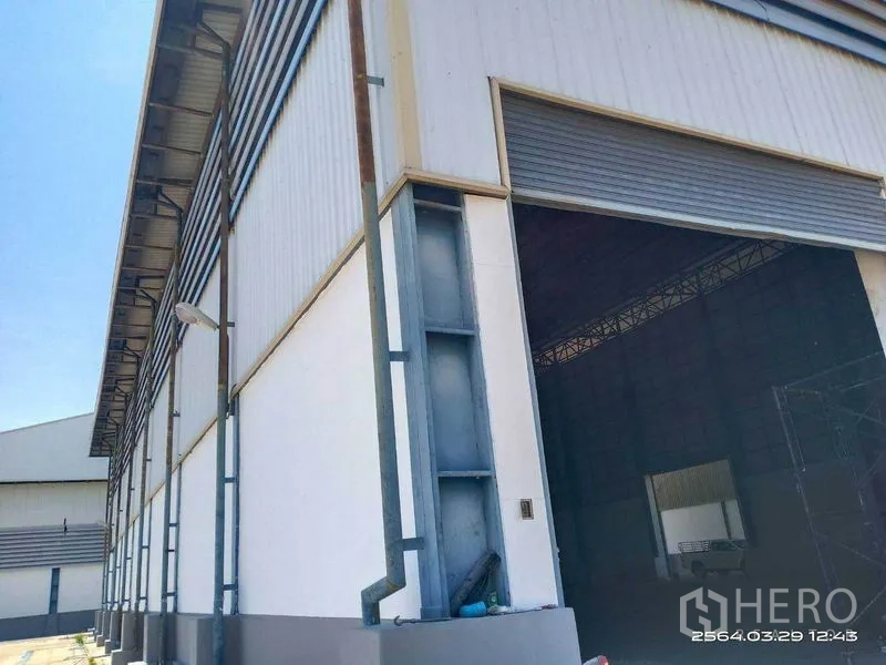 Warehouse for rent in Bang Bo, Samut Prakan - Warehouse exterior corner with large roller shutter loading door and metal cladding.
