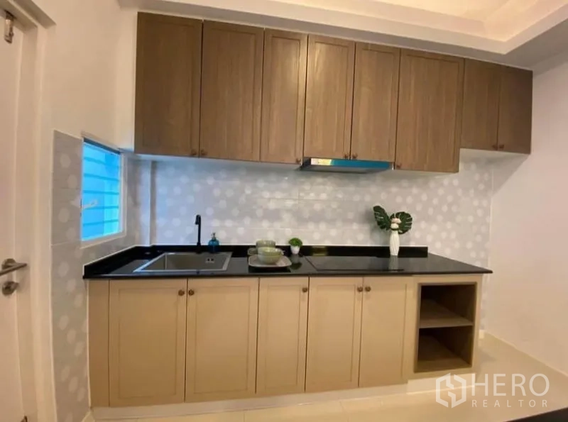Townhouse for rent in Prawet, Bangkok - Fitted kitchen with wood cabinets, black countertops and dotted tile backsplash.