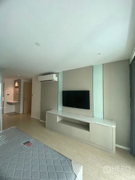 Apartment for rent in Watthana, Bangkok - Bedroom wall with mounted TV above a long console, split‑type air‑conditioner and soft neutral décor.