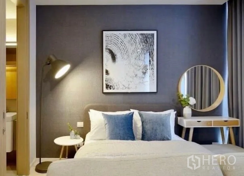 Condominium for rent in Pathum Wan, Bangkok - Bed with blue cushions, floor lamp, and dressing table against a dark accent wall.