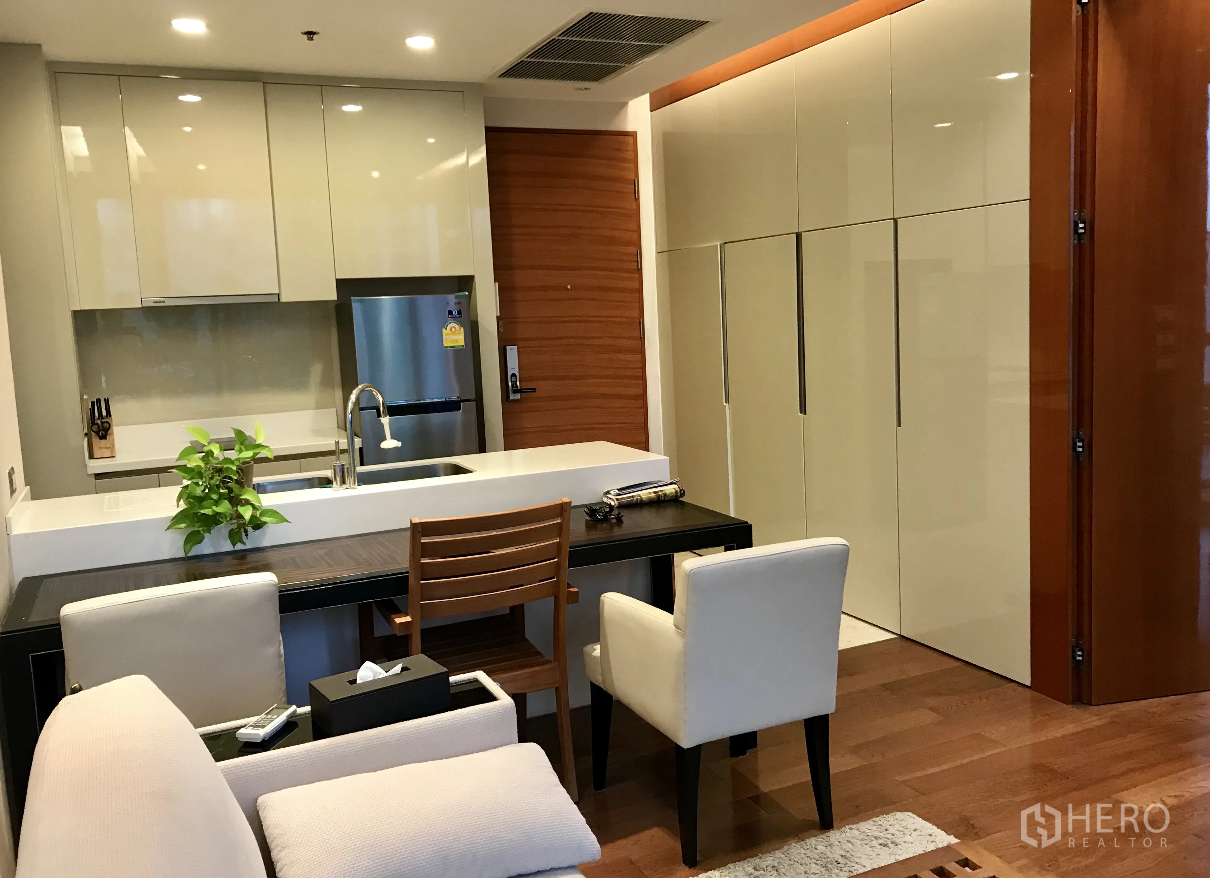 Condominium for rent or sale in Khlong Toei, Bangkok - Modern kitchenette with glossy cabinets, breakfast bar, stainless refrigerator and wooden flooring.