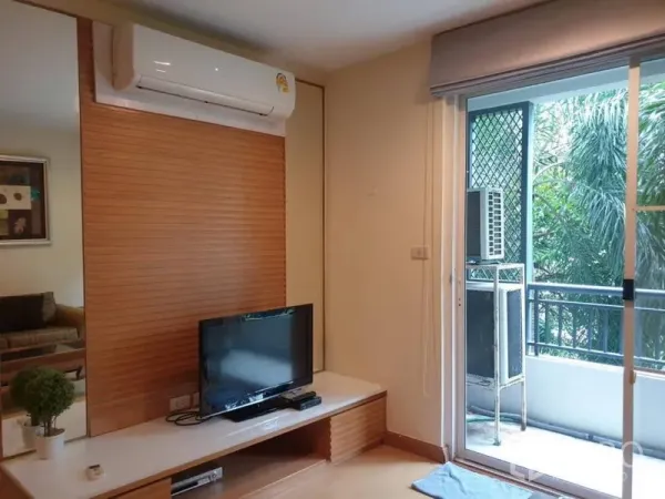 Condominium for rent in Watthana, Bangkok - Living nook with TV console and air conditioner opening to a balcony with greenery.