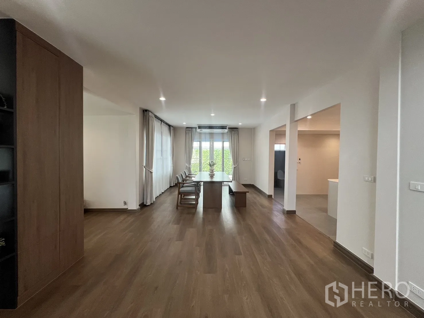 Detached House for rent in Mueang Samut Prakan, Samut Prakan - Dining room with long wooden table, large windows and curtains.