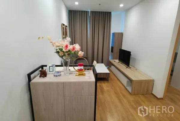 Condominium for rent in Watthana, Bangkok - Entry and living area with low TV cabinet, coffee table and decor accents on warm wood floors.