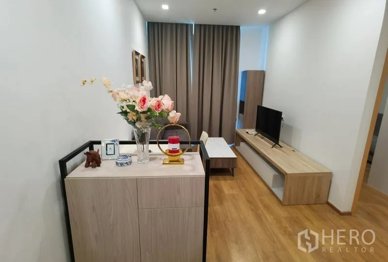公寓 出租在Watthana, Bangkok - 入口与起居区，长条电视柜、茶几与装饰摆件，温暖色木地板。