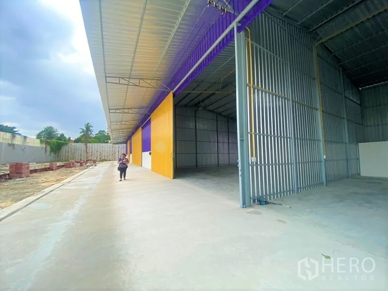 Warehouse for rent in Mueang Nonthaburi, Nonthaburi - Covered loading bay with a sliding door open, revealing the steel-framed interior and long driveway.