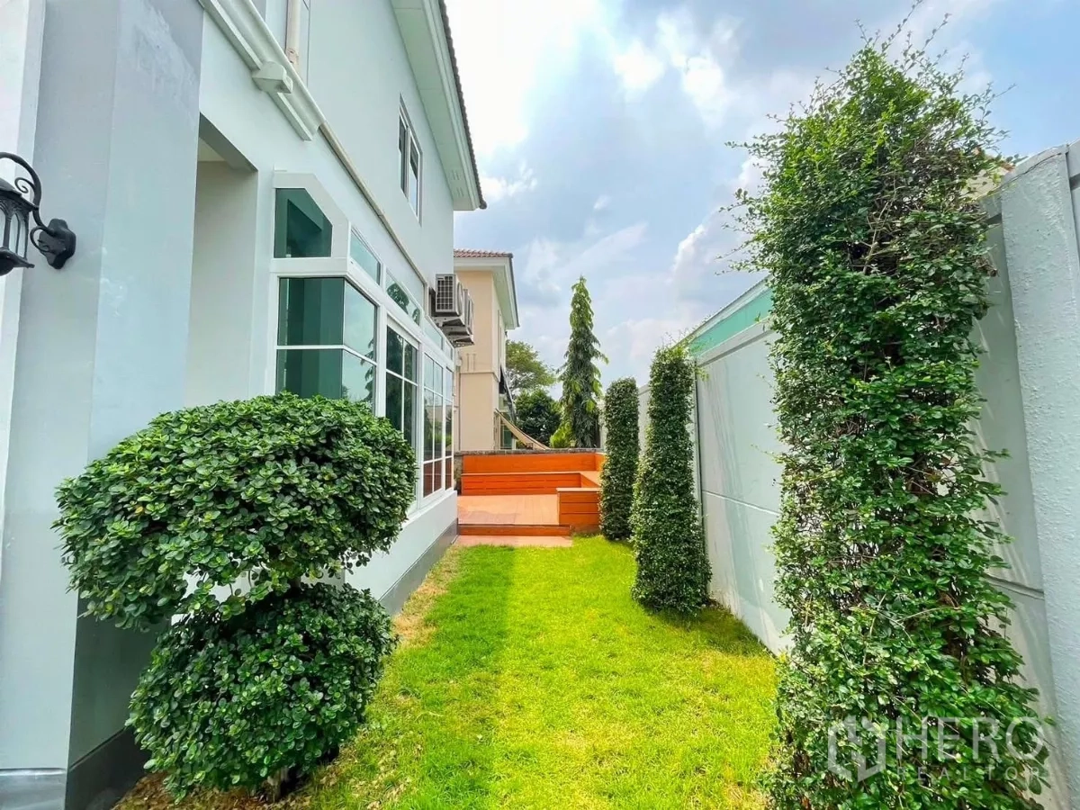 Detached House for rent in Bang Khen, Bangkok - Green side yard with trimmed hedges, lawn and a private wooden deck.