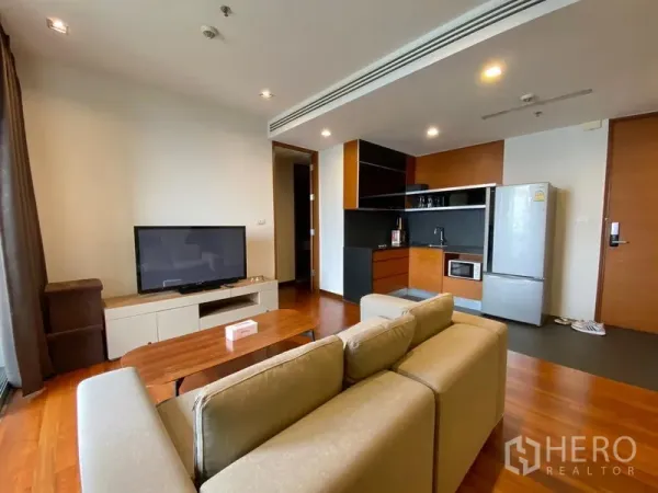 Condominium for rent - Open-plan living area with fitted kitchenette, refrigerator, sofa set and warm wood flooring.
