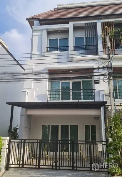 Townhouse for rent in Prawet, Bangkok - Three-storey modern townhouse exterior with balconies, a gated carport, and a white facade.