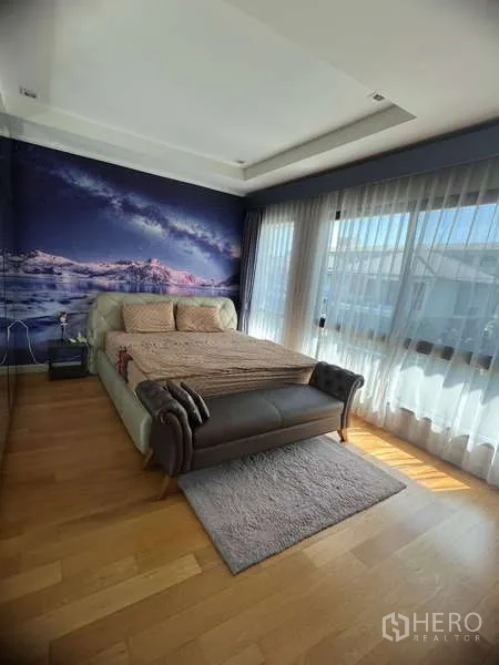 Detached House for rent or sale in Prawet, Bangkok - Master bedroom with panoramic windows, feature wall mural and bench at the foot of the bed.