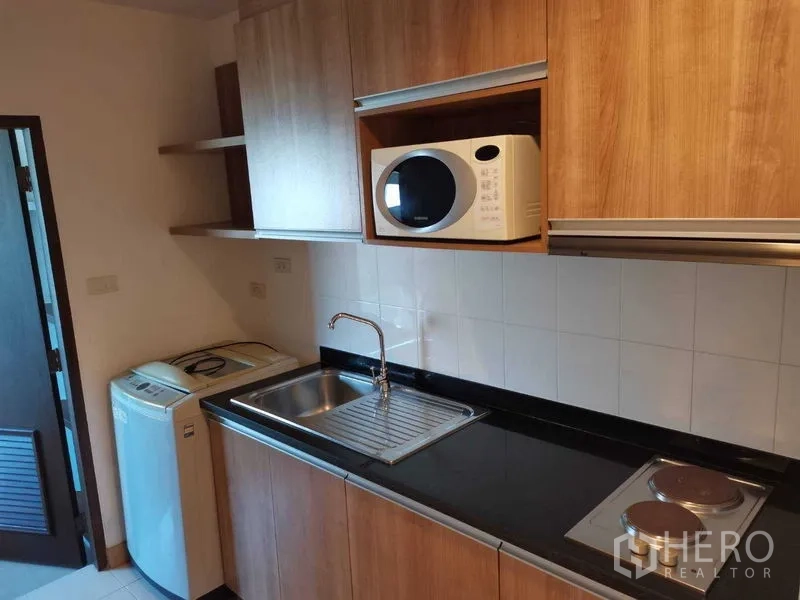 Condominium for rent in Khlong Toei, Bangkok - Separate kitchen with wooden cabinetry, sink, electric hob, microwave and washing machine.