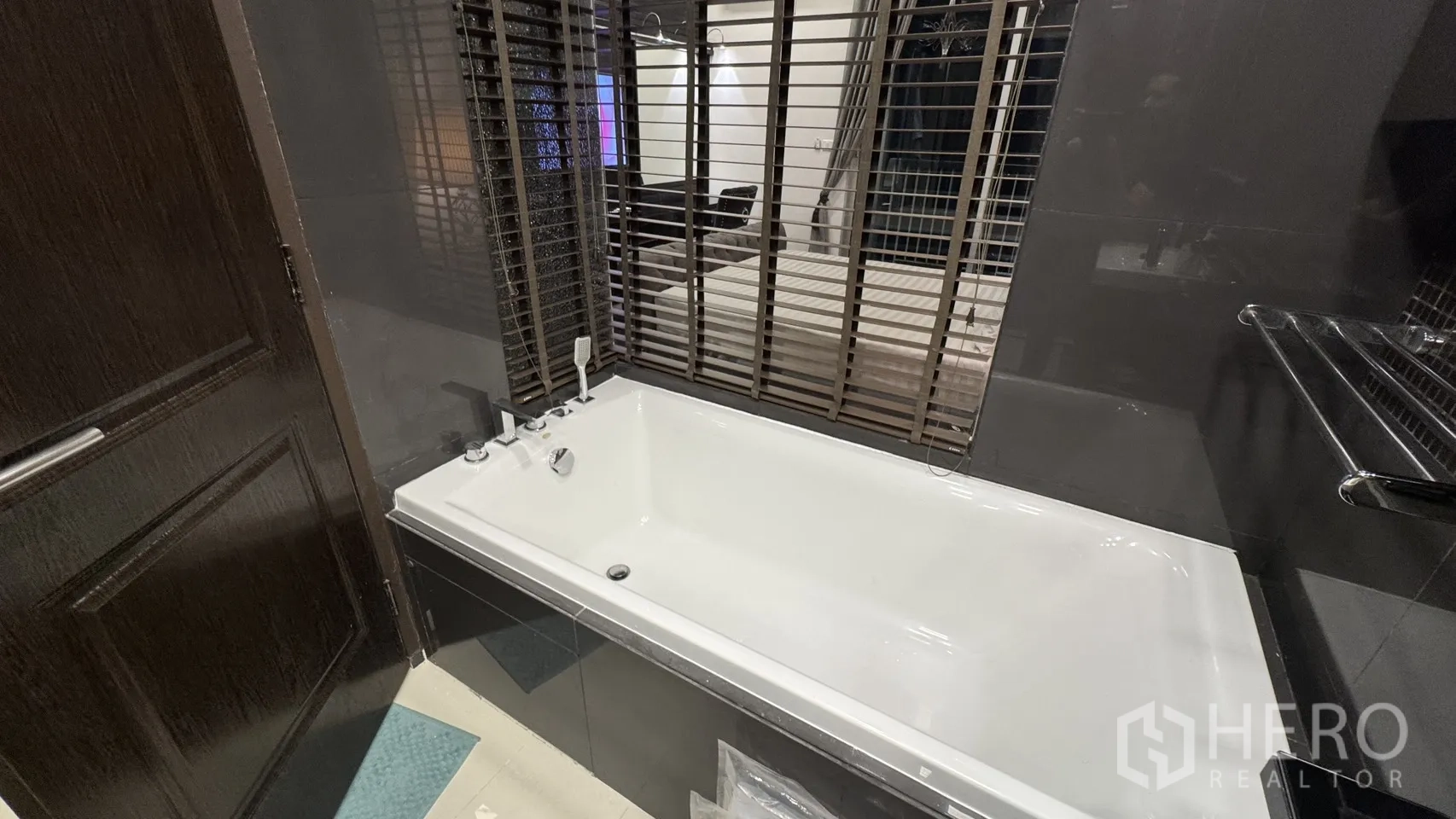 Condominium for rent or sale in Khlong Toei, Bangkok - White bathtub beside an interior window with venetian blinds facing the bedroom.