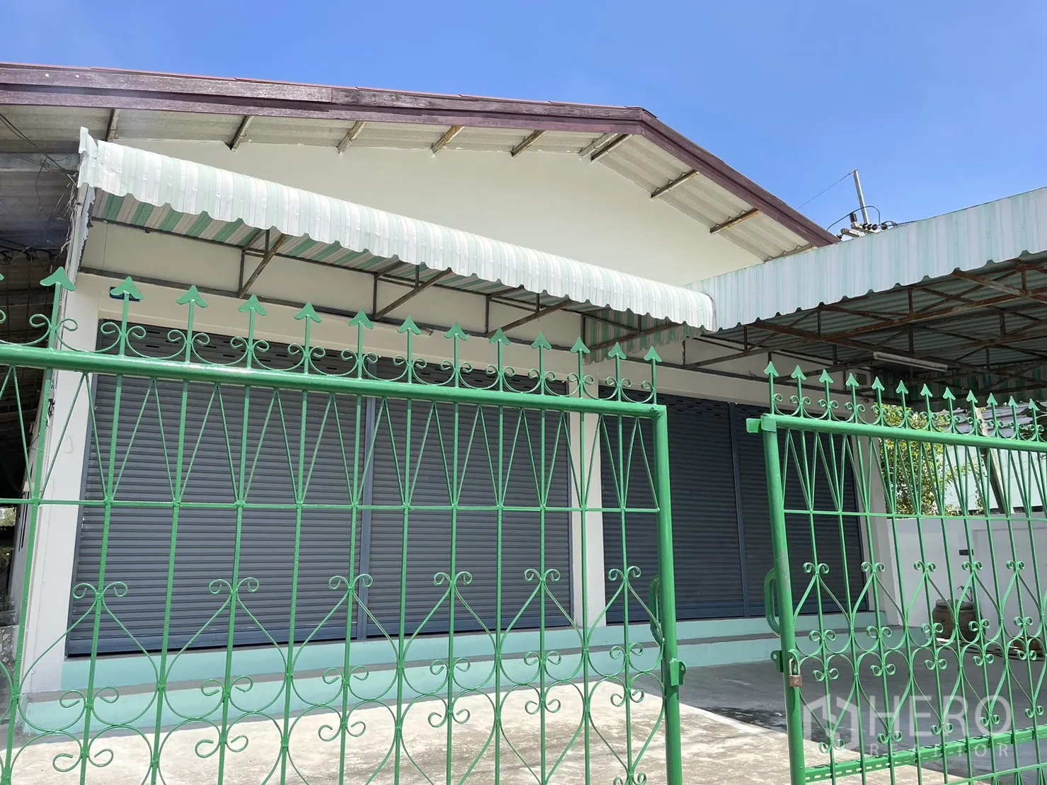 工厂 出租或出售在Pathum Thani - 临街立面，条纹遮阳篷与卷帘门，绿栏大门在前。