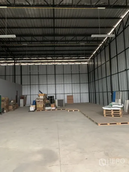 Warehouse for sale in Bang Len, Nakhon Pathom - Spacious warehouse interior with high steel truss roof, concrete floor, pallets and boxes.