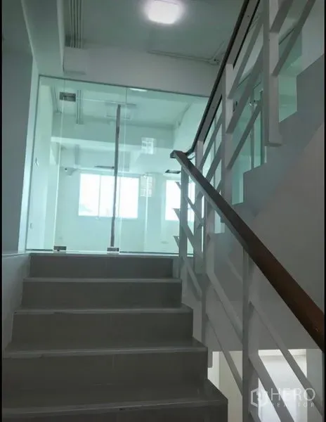 办公空间 出租在Wang Thonglang, Bangkok - 明亮的室内楼梯与白色栏杆，通往曼谷旺通朗的玻璃隔间办公楼层。