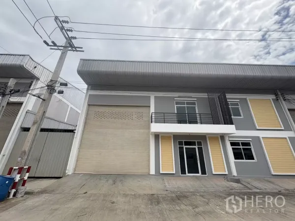 Factory for rent in Phra Samut Chedi, Samut Prakan - Modern two-storey factory facade with a wide roller shutter, balcony and concrete loading apron.