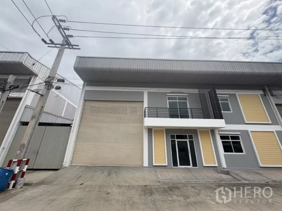 Factory for rent in Phra Samut Chedi, Samut Prakan - Modern two-storey factory facade with a wide roller shutter, balcony and concrete loading apron.