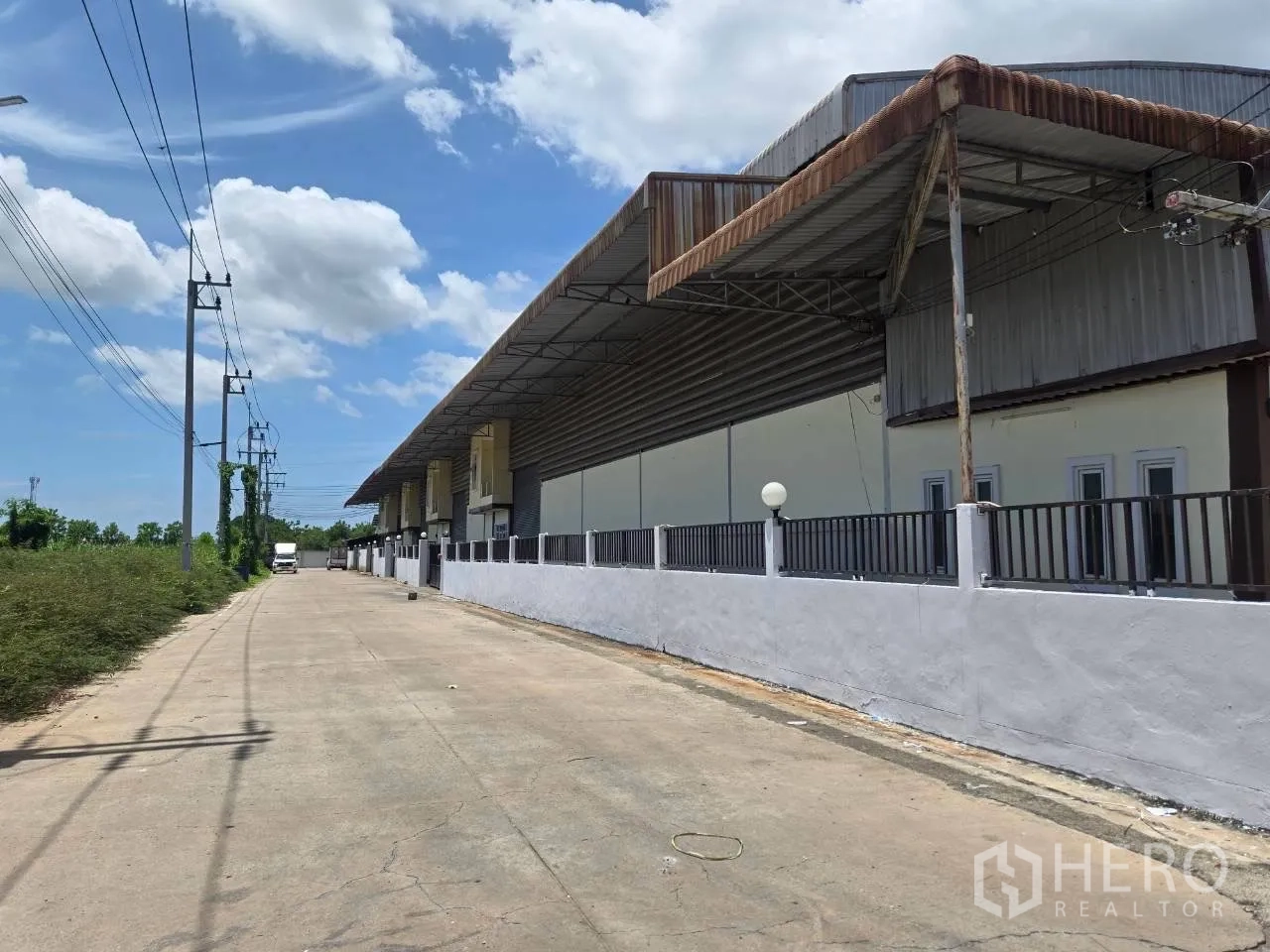 Warehouse for rent or sale in Mueang Samut Sakhon, Samut Sakhon - Facade of the warehouse showing an extended canopy roof and fenced boundary along the road.
