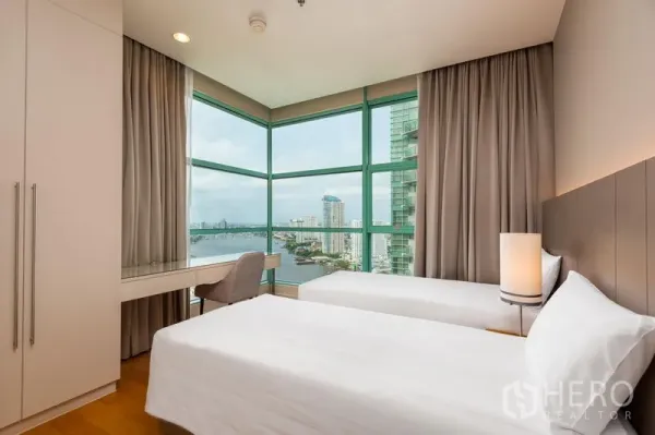 Condominium for rent in Bang Kho Laem, Bangkok - Corner twin bedroom with desk and floor‑to‑ceiling windows showcasing a river and city view.