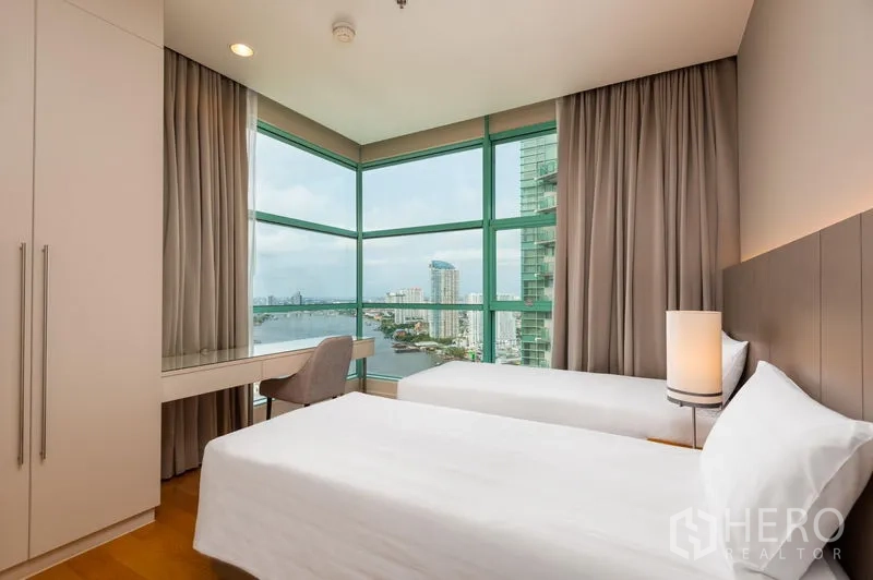 Condominium for rent in Bang Kho Laem, Bangkok - Corner twin bedroom with desk and floor‑to‑ceiling windows showcasing a river and city view.