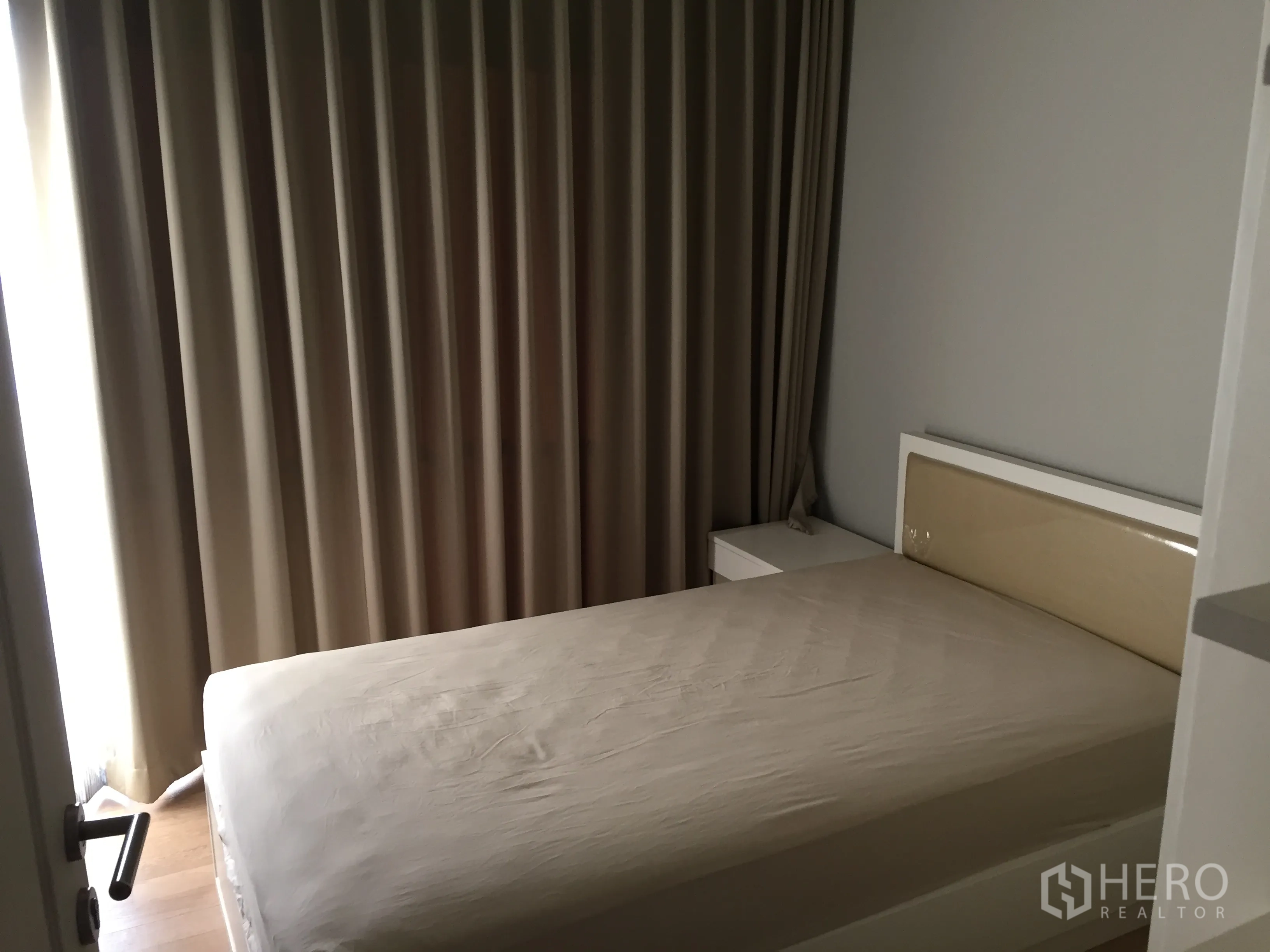 Condominium for rent in Bangkok - Cozy bedroom with double bed, bedside table, and floor-to-ceiling blackout curtains.