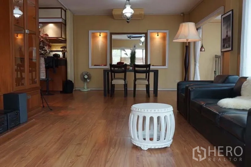 Detached House for rent in Suan Luang, Bangkok - Open-plan lounge and dining area with wooden floor, pendant lights and a black dining set.
