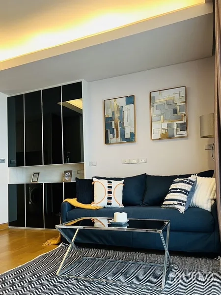 公寓 出租在Khlong Toei, Bangkok - 温馨会客角，海军蓝沙发、玻璃茶几与装饰画。