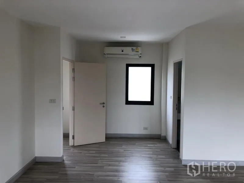 Townhouse for rent or sale in Saphan Sung, Bangkok - Upper-floor bedroom with wood-look flooring, window, air conditioner and ensuite door.