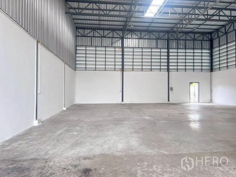 Warehouse for rent in Lam Luk Ka, Pathum Thani - Storage hall showing ventilated upper wall panels and a side exit door.