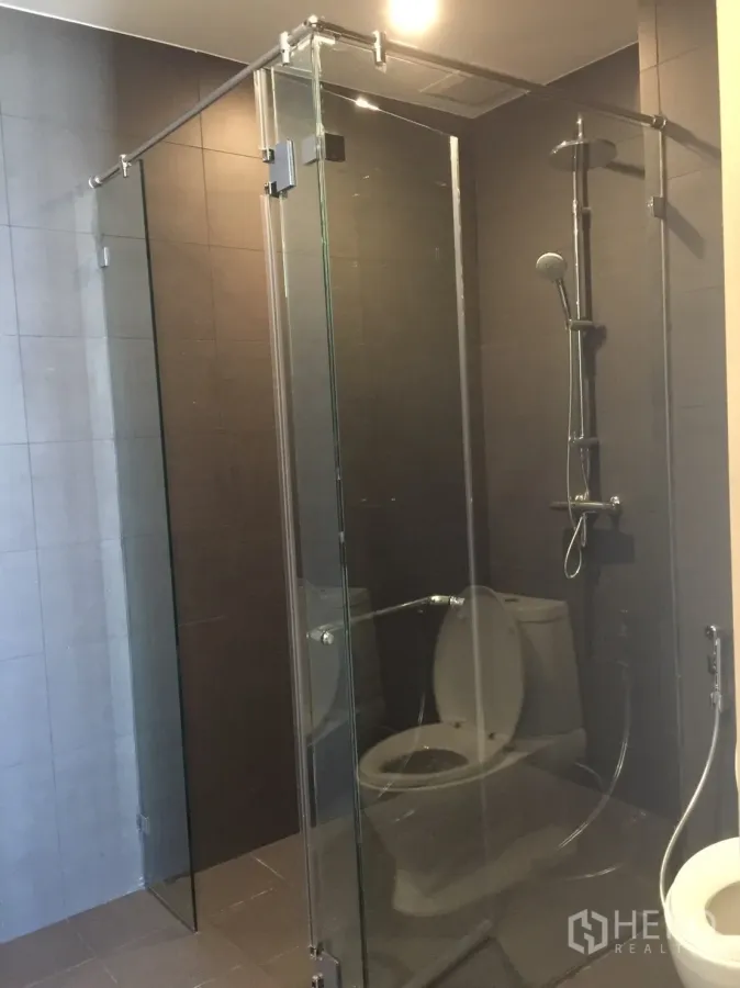 Condominium for sale in Pathum Wan, Bangkok - Modern bathroom with frameless glass shower and rain shower on dark tiles.