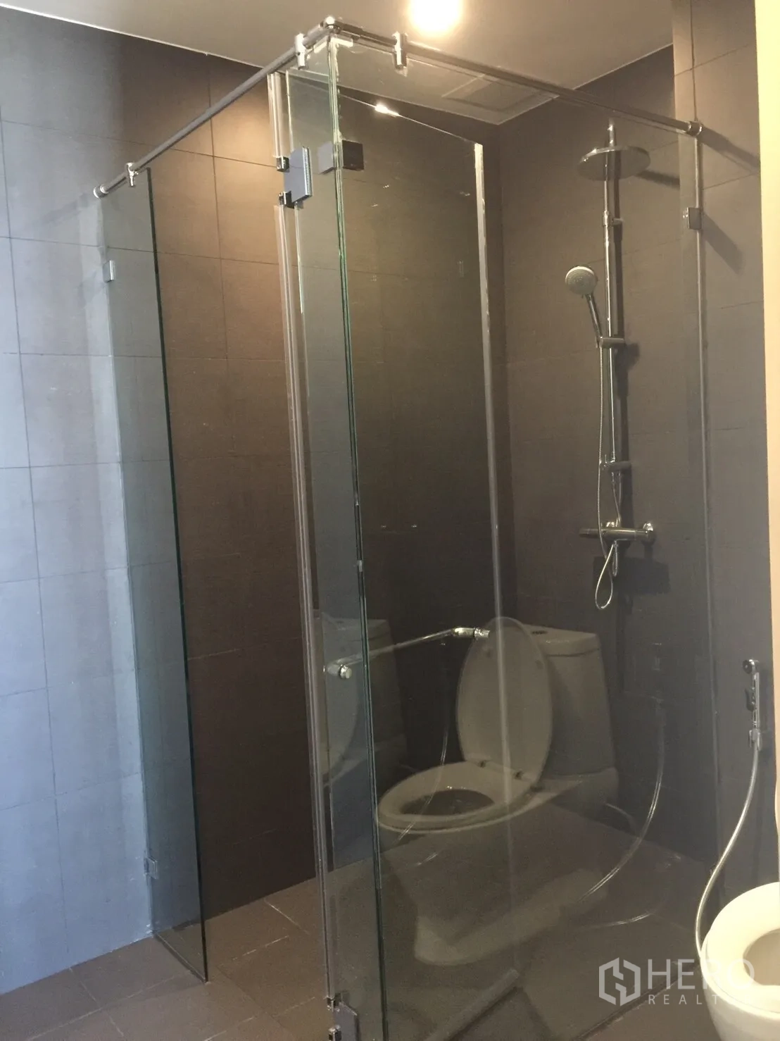 Condominium for sale in Pathum Wan, Bangkok - Modern bathroom with frameless glass shower and rain shower on dark tiles.