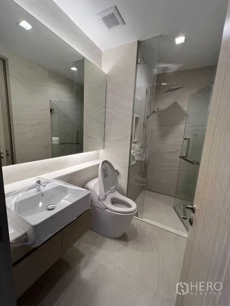 Condominium for rent in Ratchathewi, Bangkok - Modern bathroom with glass shower, large mirror and sanitary ware.