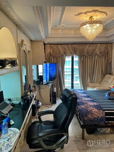Condominium for sale in Khlong Toei, Bangkok - Bedroom with chandelier, heavy drapes, balcony door and built-in vanity with TV.