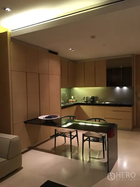 Condominium for rent or sale in Bang Rak, Bangkok - Open-plan kitchen with light wood cabinetry, black stone counters and two-seat dining table.
