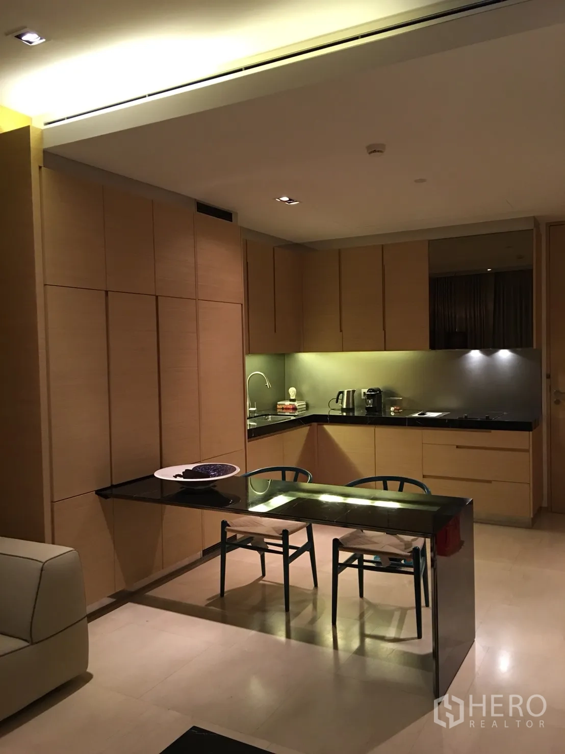 Condominium for rent or sale in Bang Rak, Bangkok - Open-plan kitchen with light wood cabinetry, black stone counters and two-seat dining table.