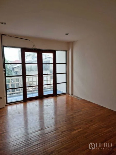 联排别墅 出租在Wang Thonglang, Bangkok - 卧室，浅色墙面与木地板，阳台玻璃门采光充足。