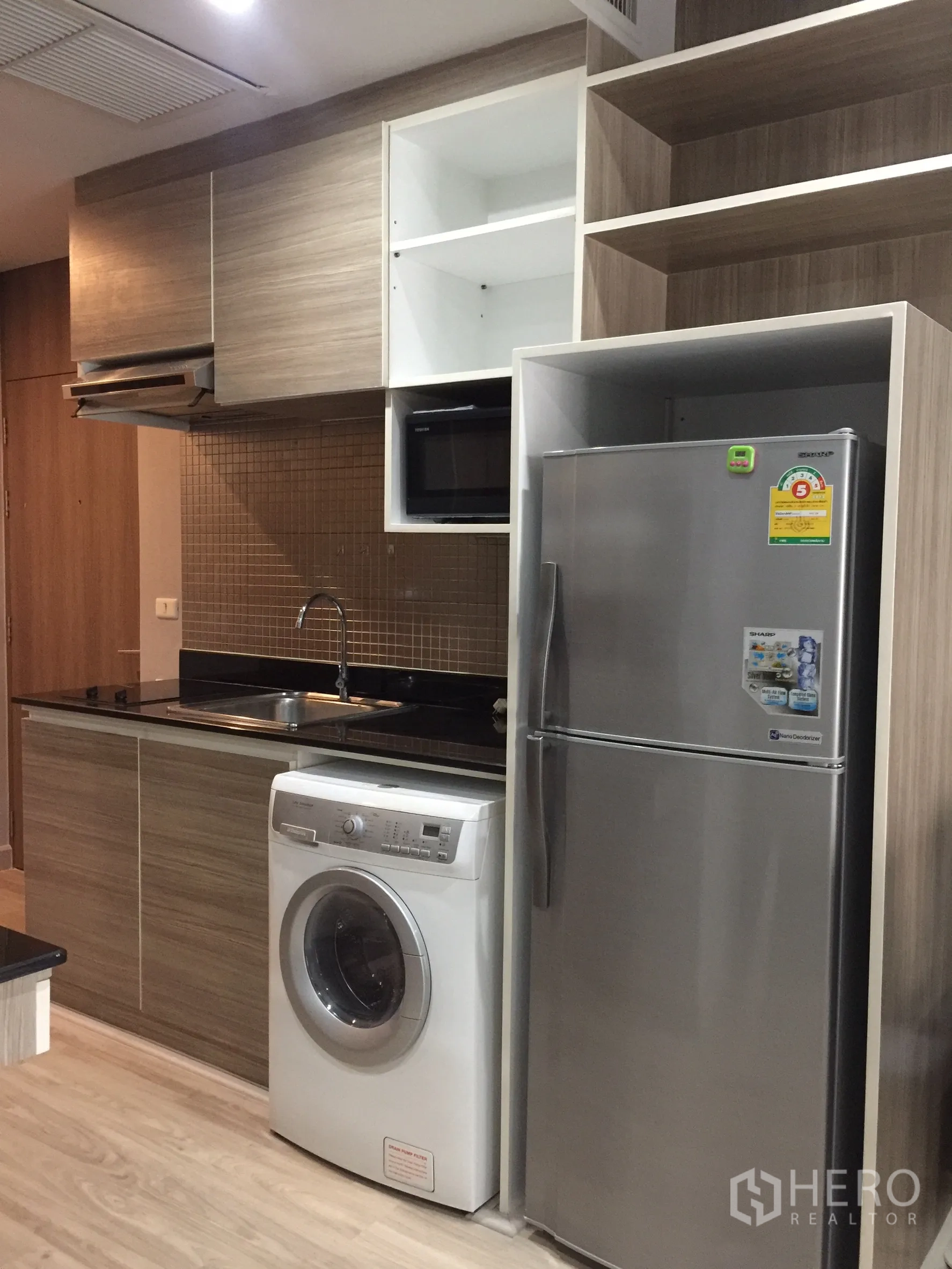 Condominium for rent or sale in Bangkok - Compact kitchenette with fridge, washing machine, sink and wood cabinets.